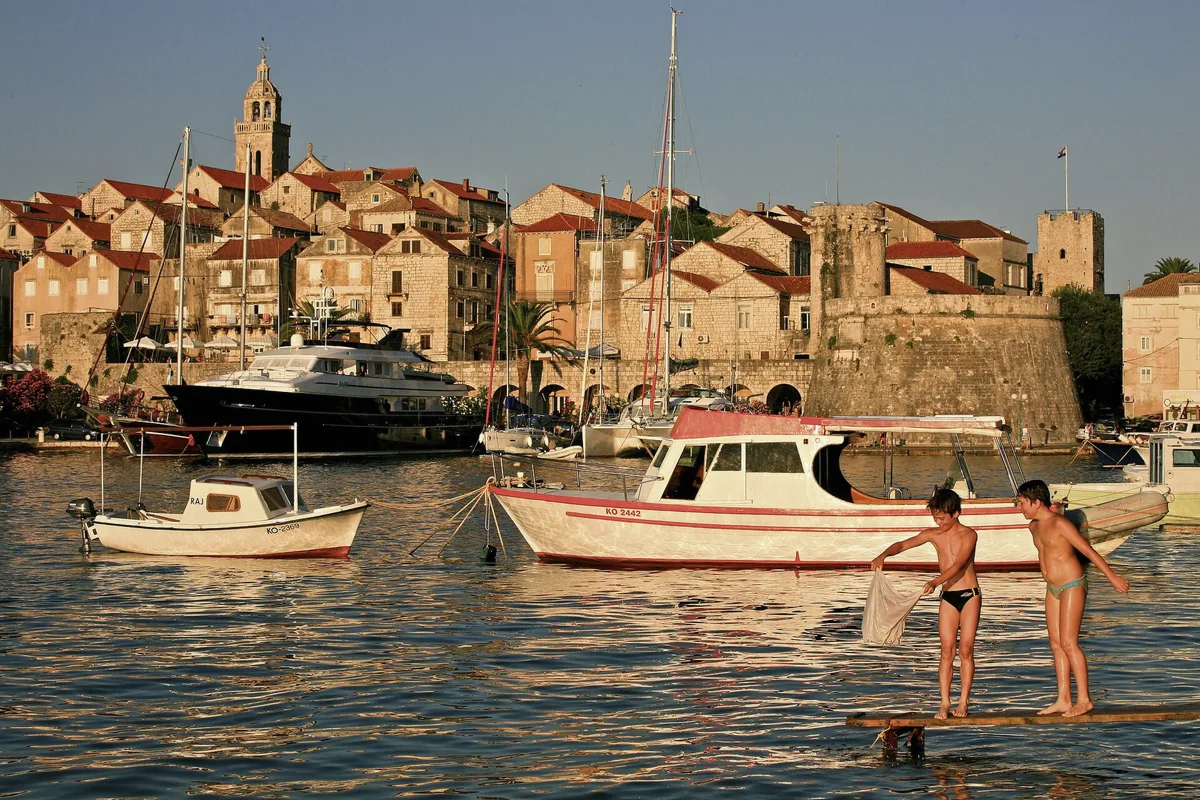 Children playing on a pontoon beside moored boats in Korcula Town harbour in Croatia at golden hour